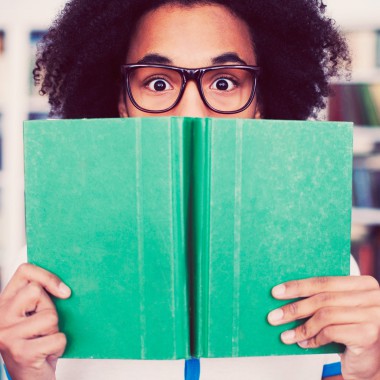 Boy wearing glasses hiding behind book