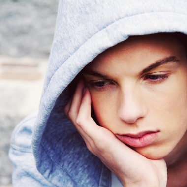 Teenage boy wearing grey hoodie looking fed up