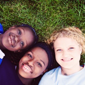 Three girls lying on the grass smiling at the camera